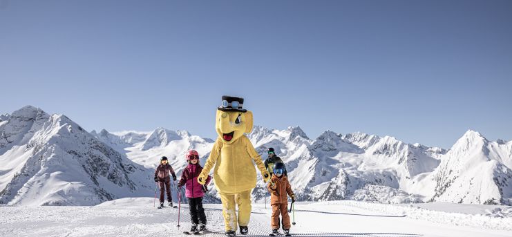 Kinder mit Maskottchen auf der Piste im Familienskigebiet